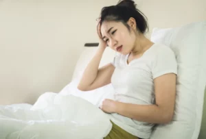 Asian women suffering from abdominal pain while lying on bed